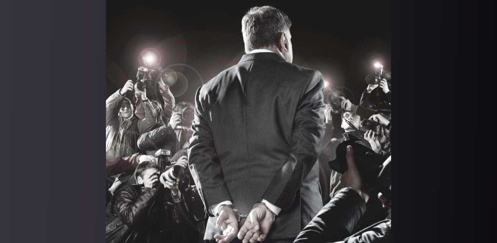 A handcuffed man facing  the paparazzi with flashing cameras